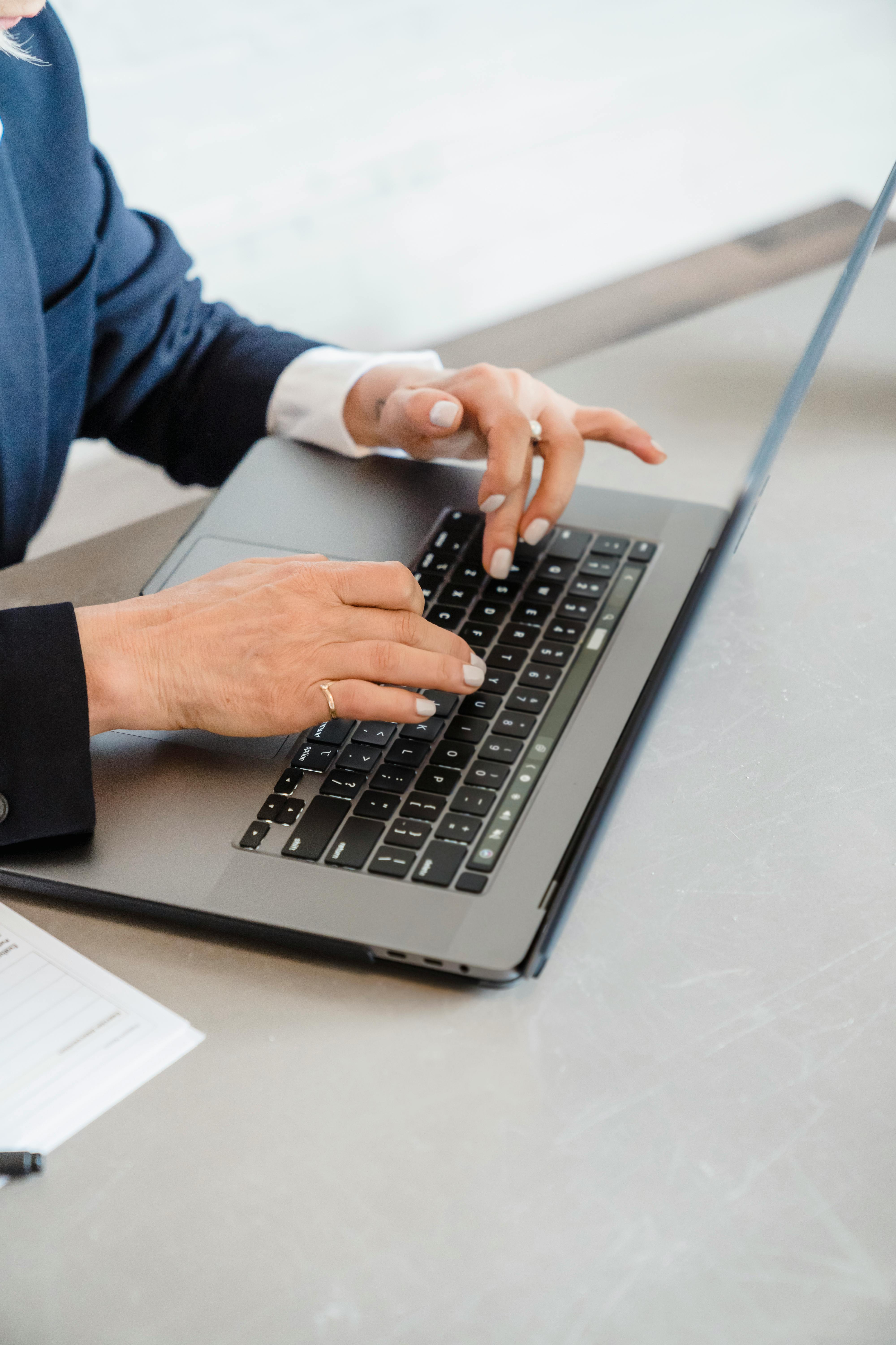 Close-up of a business professional's hands typing on a laptop in a modern office setting.